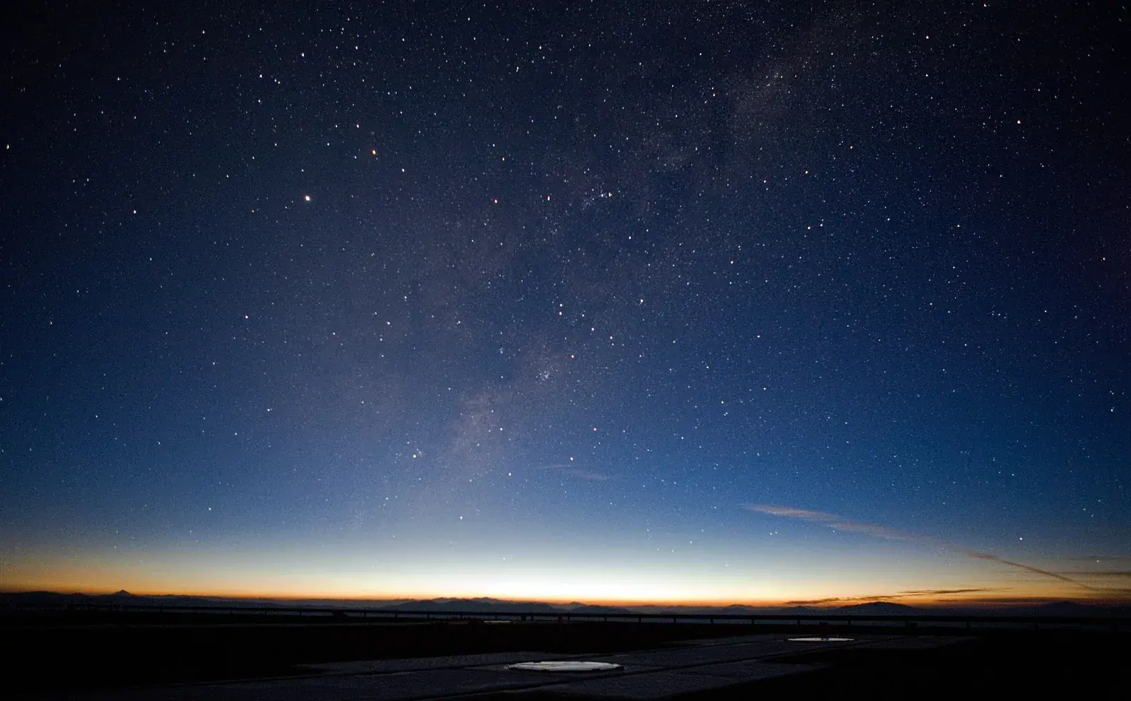 Starry pre-dawn sky over a flat observatory platform, with an orange glow along the eastern horizon line