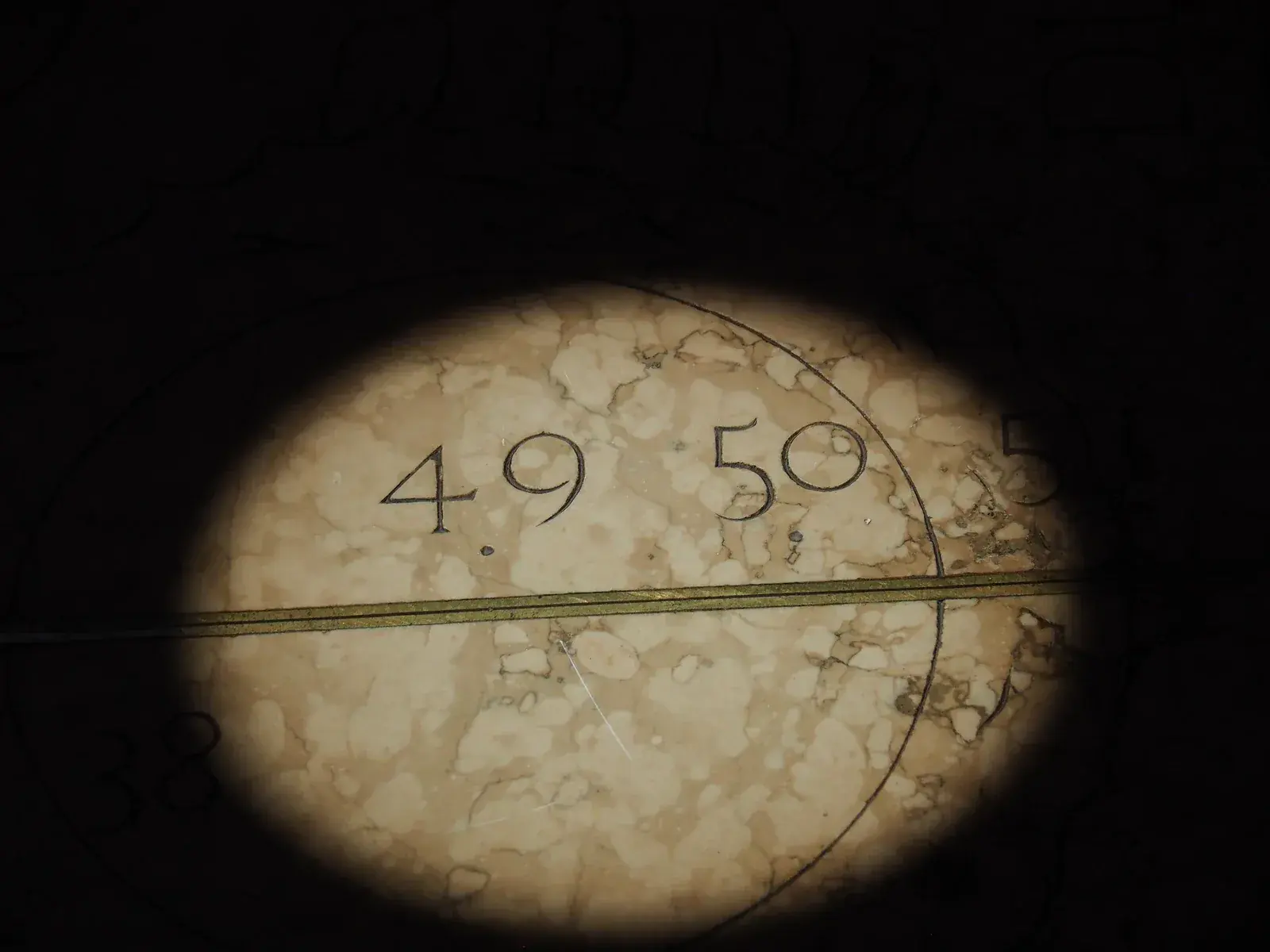 Oval patch of sunlight on a marble floor, cut through by a brass line, with carved numbers 49 and 50