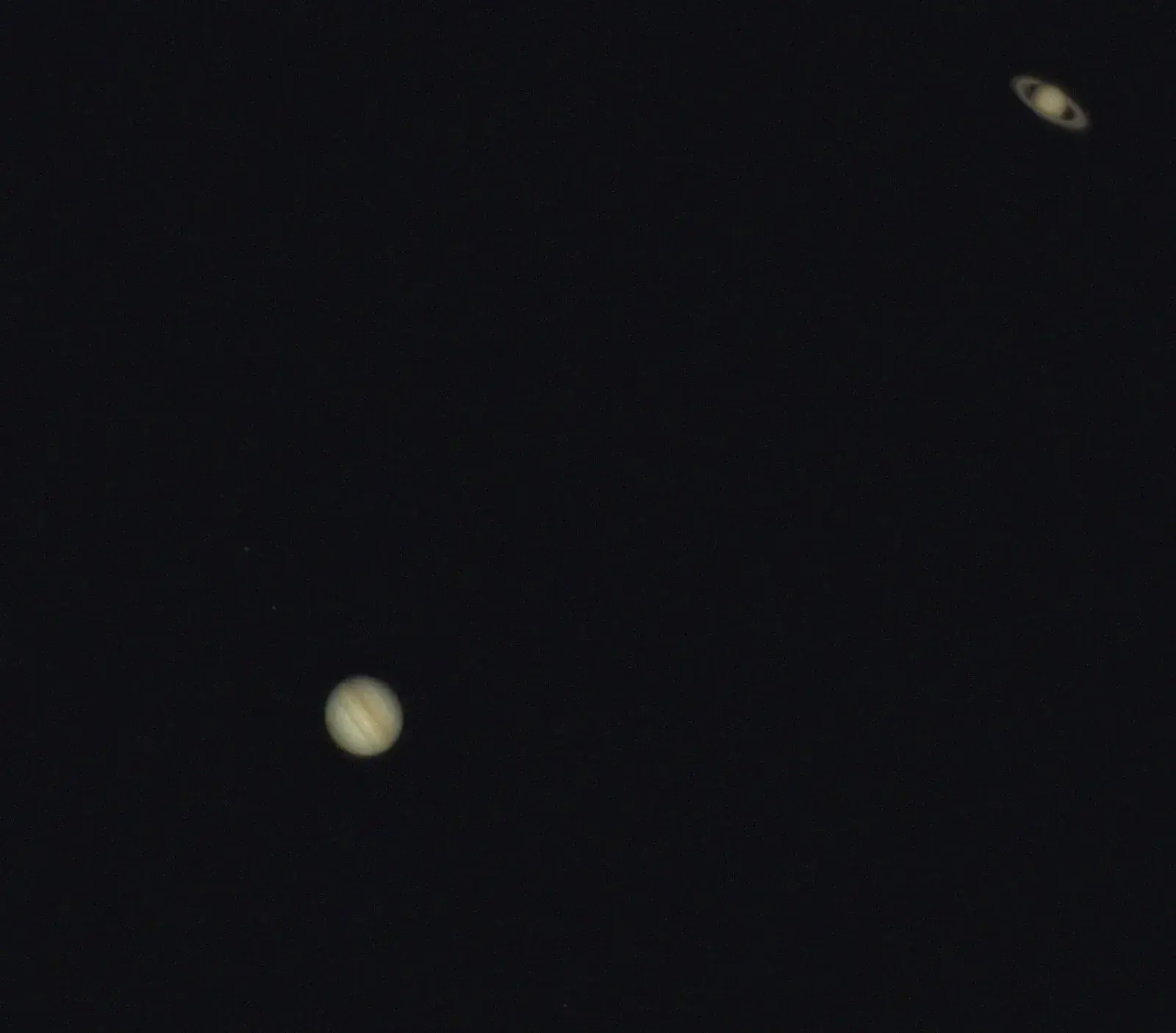 Telescope view of banded Jupiter at lower left and ringed Saturn at upper right in one dark field