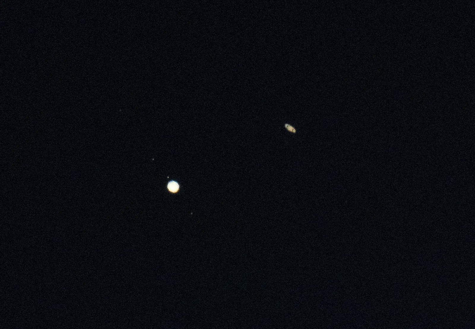 Telescopic photo of bright Jupiter with faint moons at lower left and small ringed Saturn at upper right