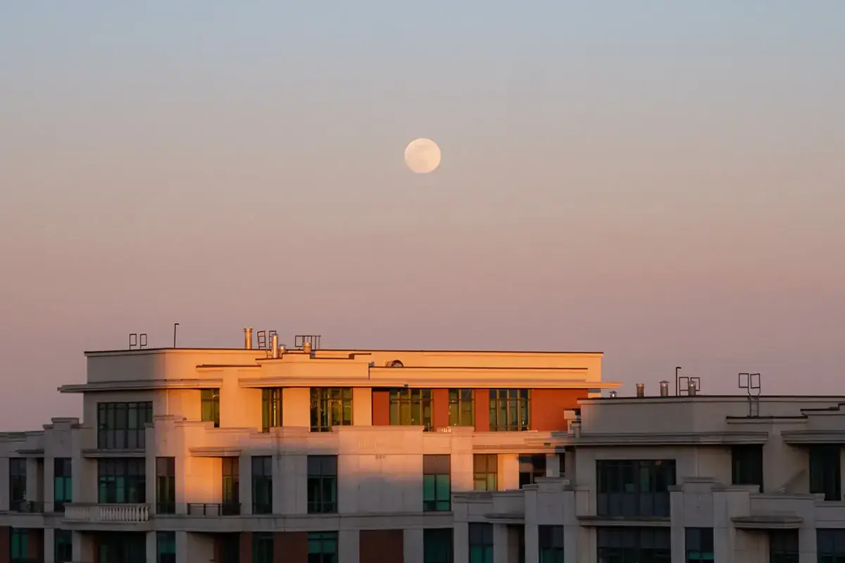 A full Moon rising over apartment buildings at pink dusk