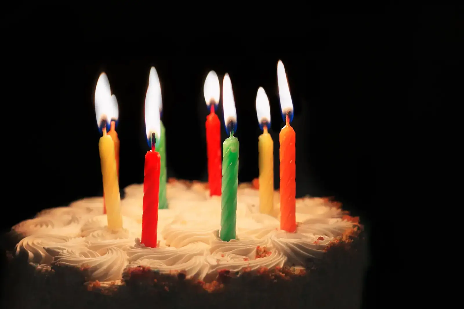 Lit birthday candles glowing on a cake in the dark