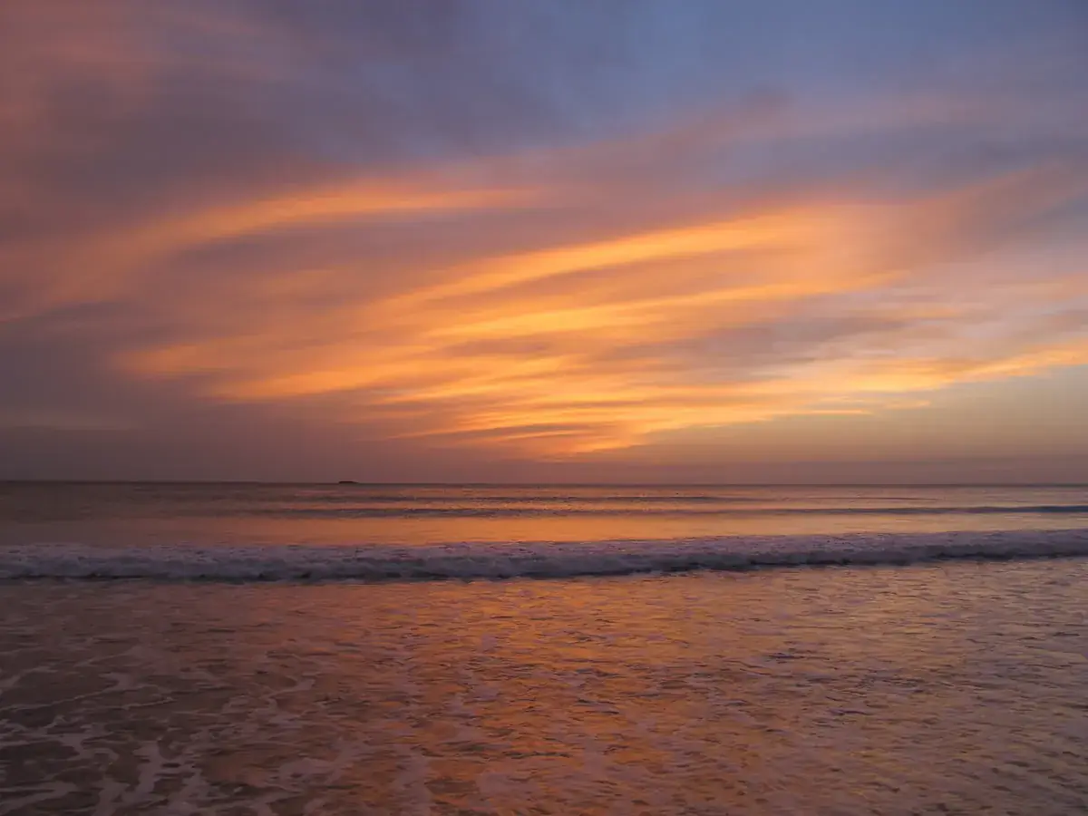 Foamy waves rolling in under an orange sunset (Sagittarius and Pisces compatibility)