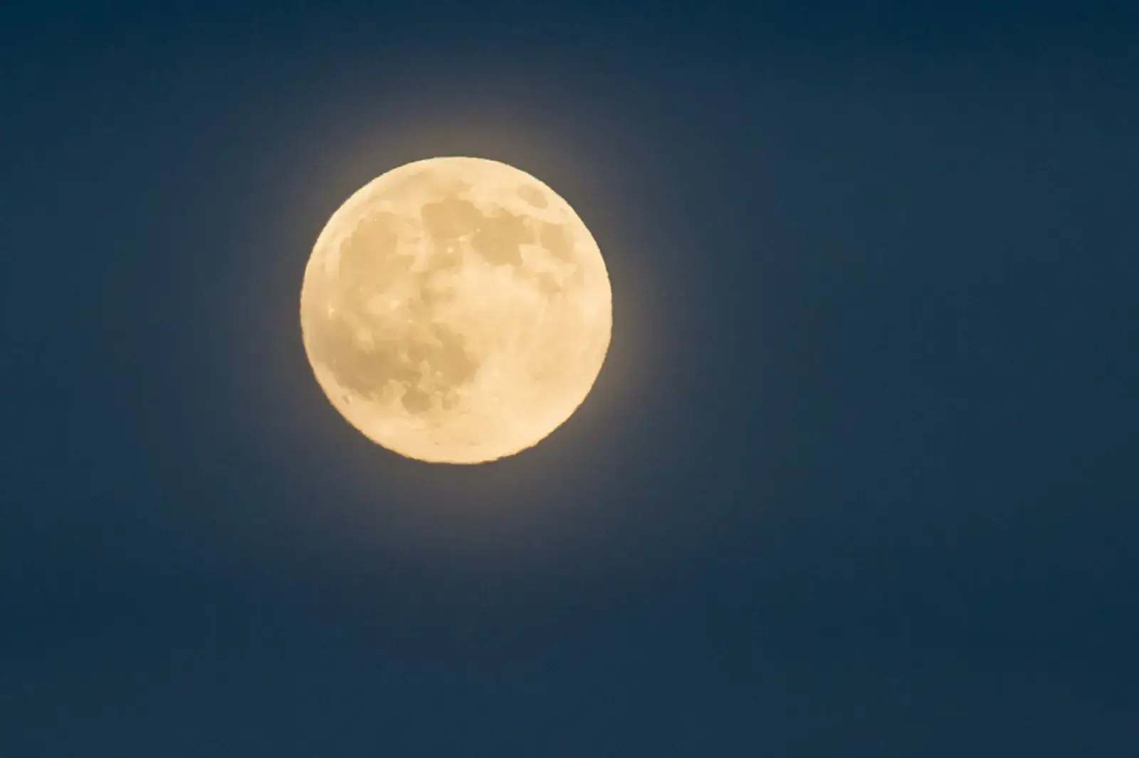 A full Moon glowing in a deep blue sky
