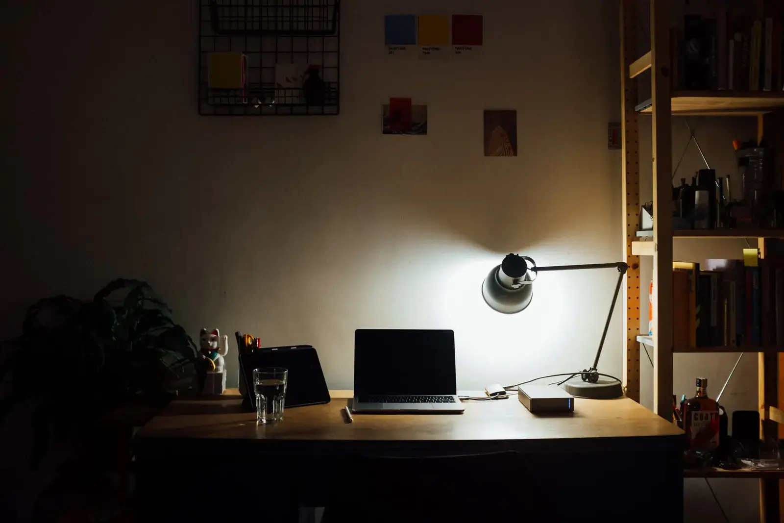 A desk lamp glowing over a laptop in a dark, book-lined study