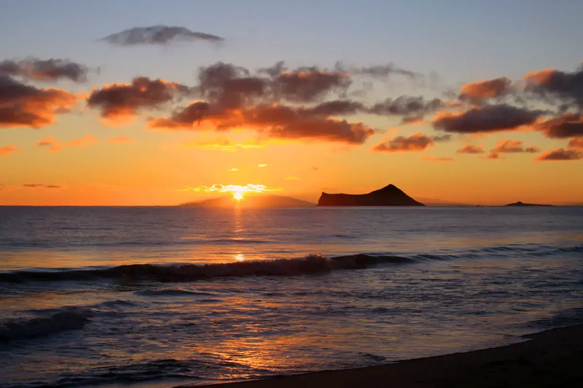 The sun on the sea horizon beside an island, under orange clouds (Leo and Sagittarius compatibility)