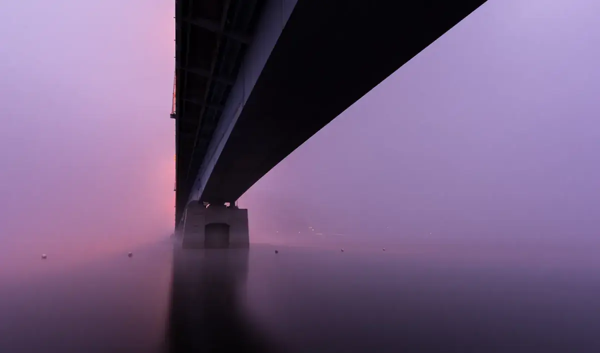 The underside of a long bridge reaches across purple water at dusk (Libra and Scorpio compatibility)