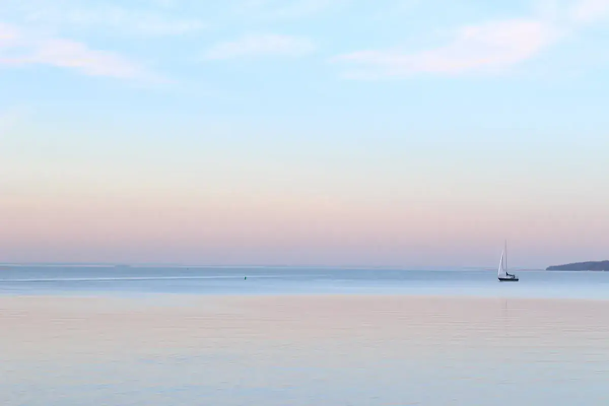 A tiny sailboat on a calm sea under a pastel evening sky (Libra and Pisces compatibility)