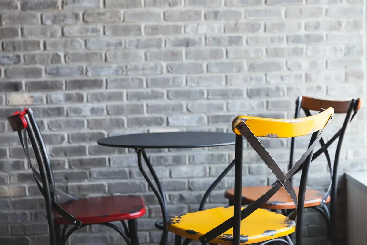 Two mismatched cafe chairs, one yellow and one red, at a small table by a brick wall (Virgo and Libra compatibility)