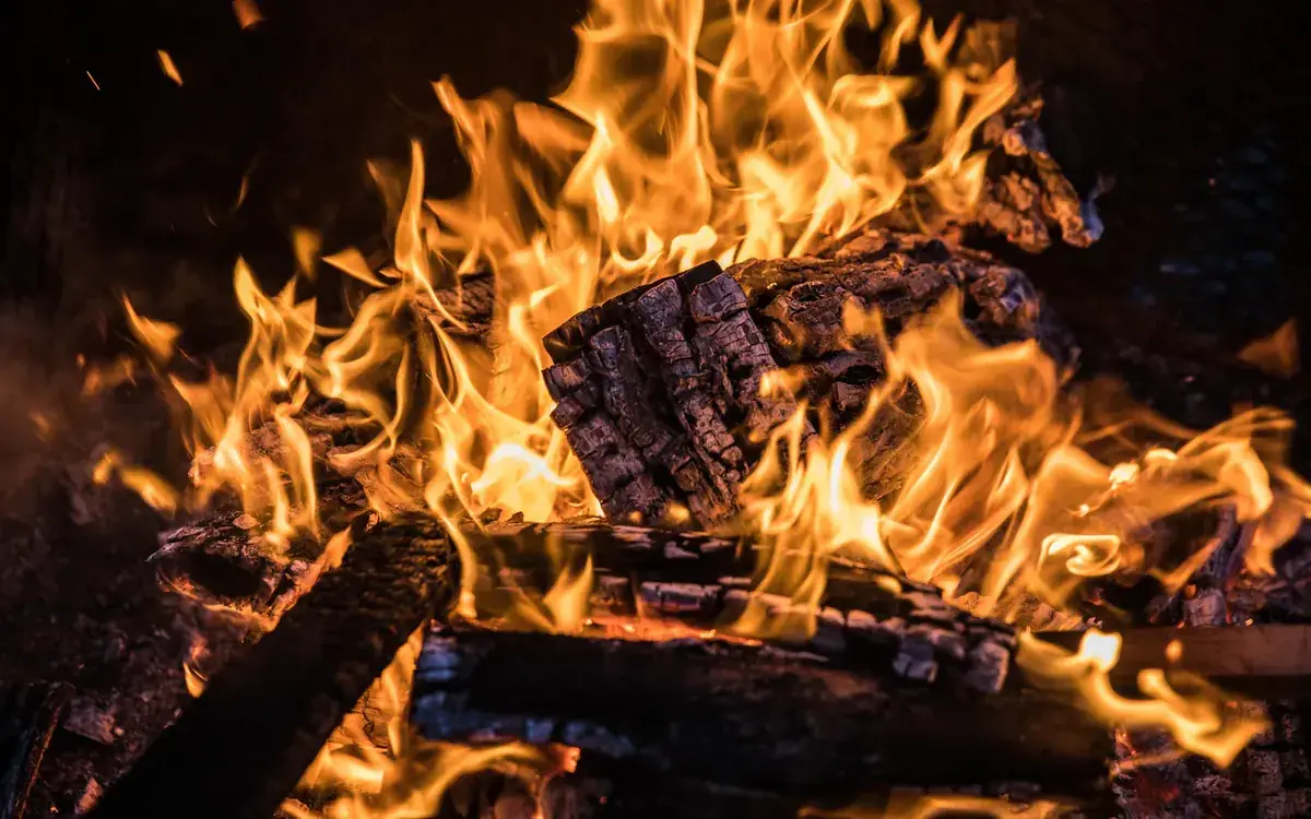 Tall flames leap from a stacked log fire against a dark background (Aries and Leo compatibility)