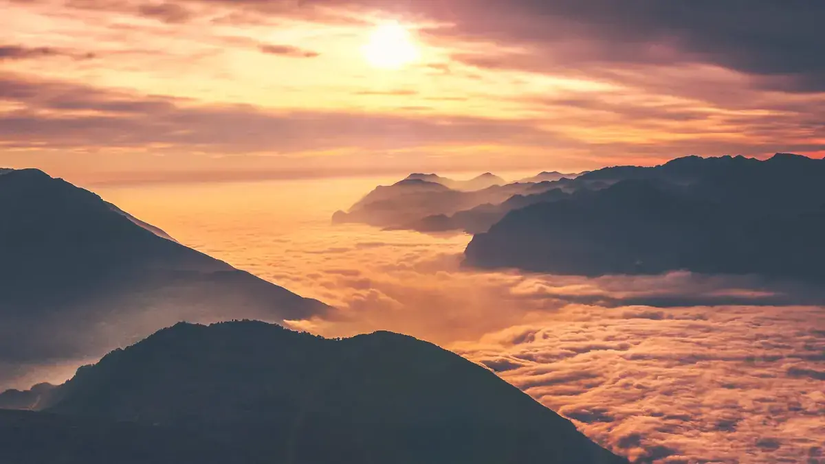 A sea of clouds fills the valleys between dark ridges at sunset (Aquarius and Pisces compatibility)