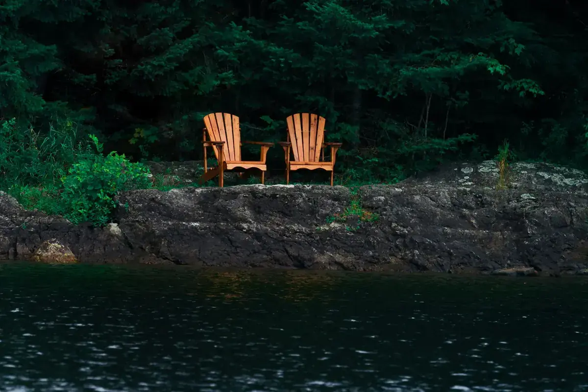 Two orange Adirondack chairs sit on a rocky shore above dark, calm water (Taurus and Cancer compatibility)