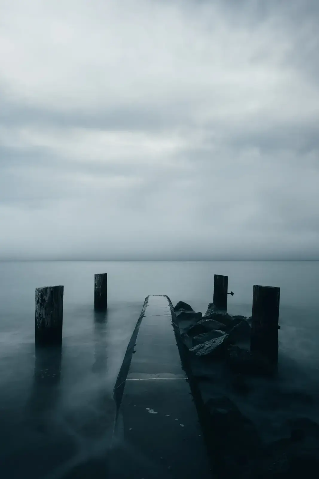 Weathered dock posts stand in dark, still water under a heavy grey sky (Gemini and Scorpio compatibility)