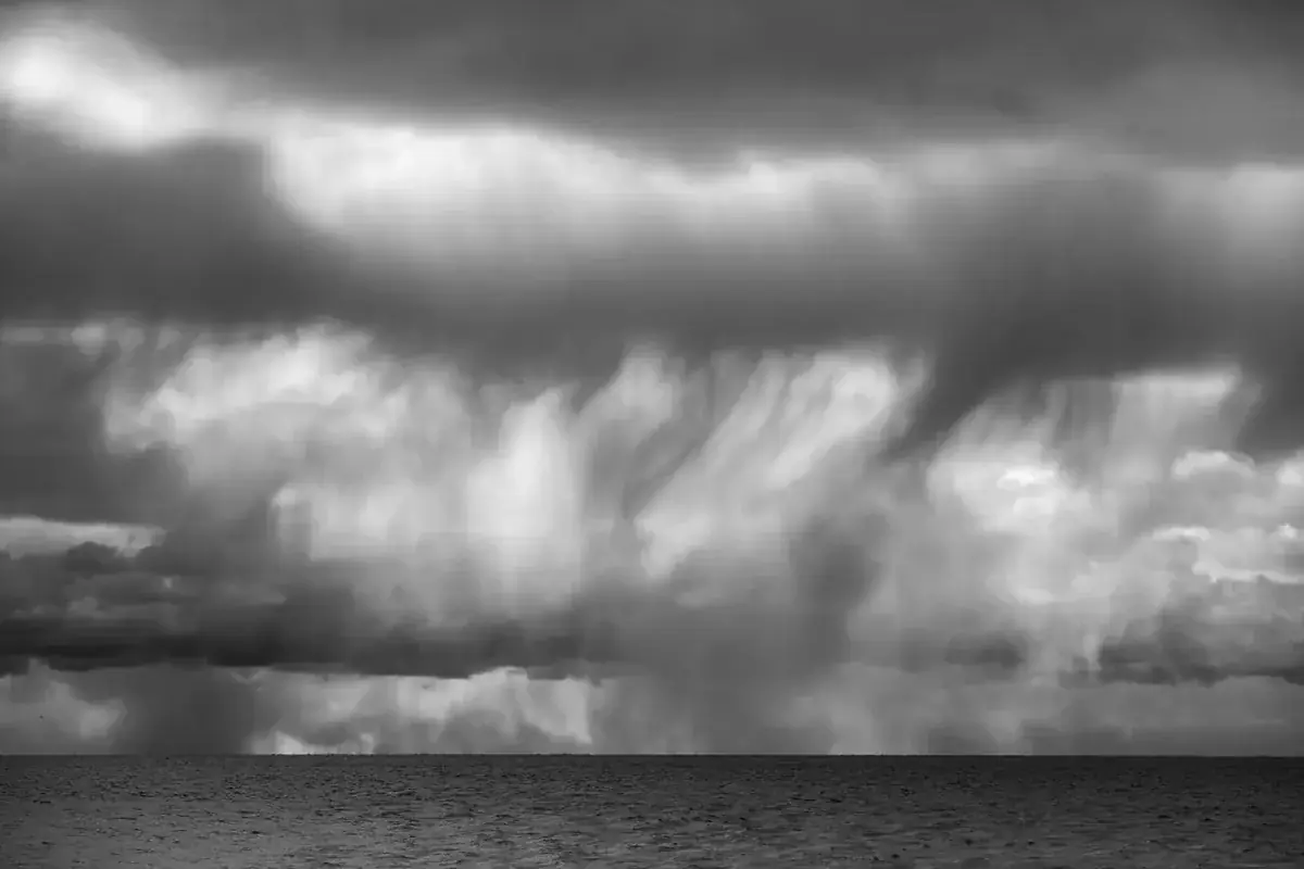 A curtain of rain sweeps across the sea beneath dramatic clouds, in black and white (Gemini and Pisces compatibility)