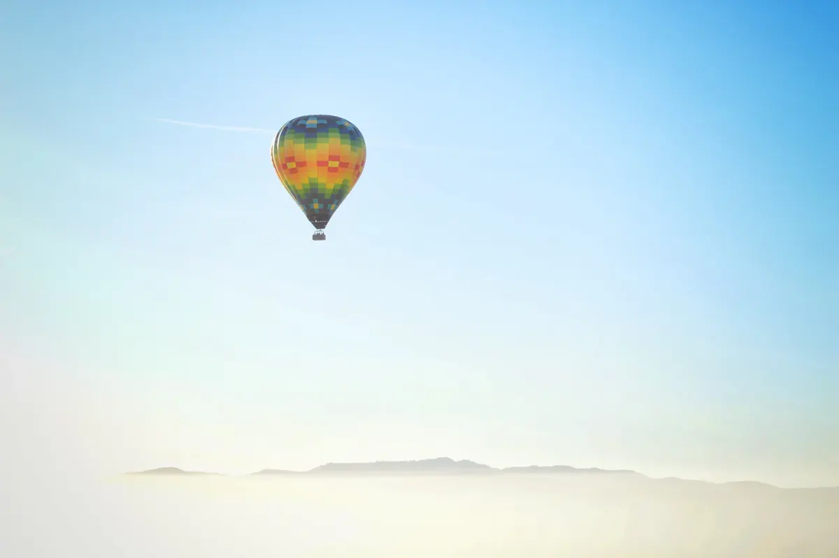 A single striped hot-air balloon floats in a clear, pale sky (Sagittarius and Aquarius compatibility)