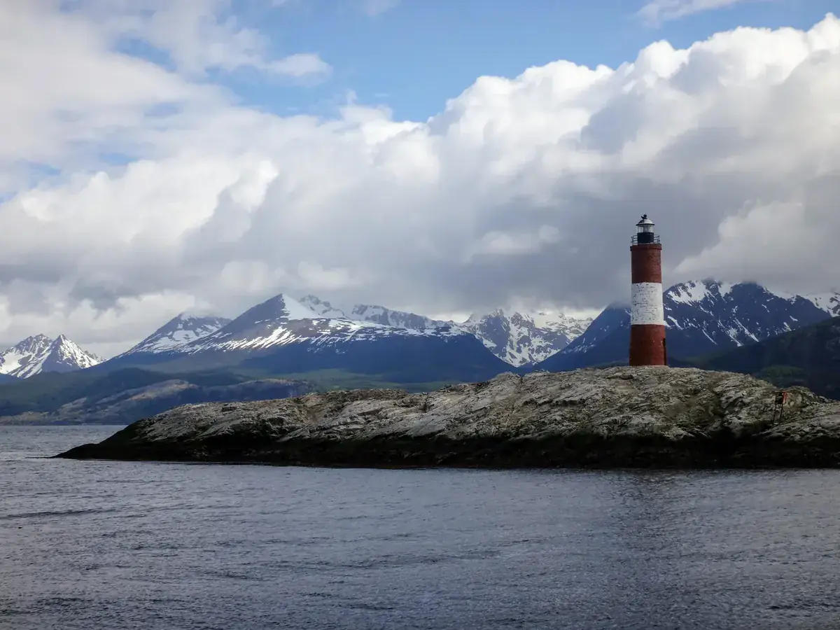 A red-and-white lighthouse on a small island below snow-capped mountains (Cancer and Capricorn compatibility)