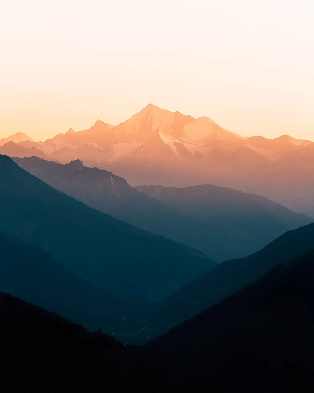 Alpenglow lights a distant summit pink above dark blue valleys (Leo and Capricorn compatibility)
