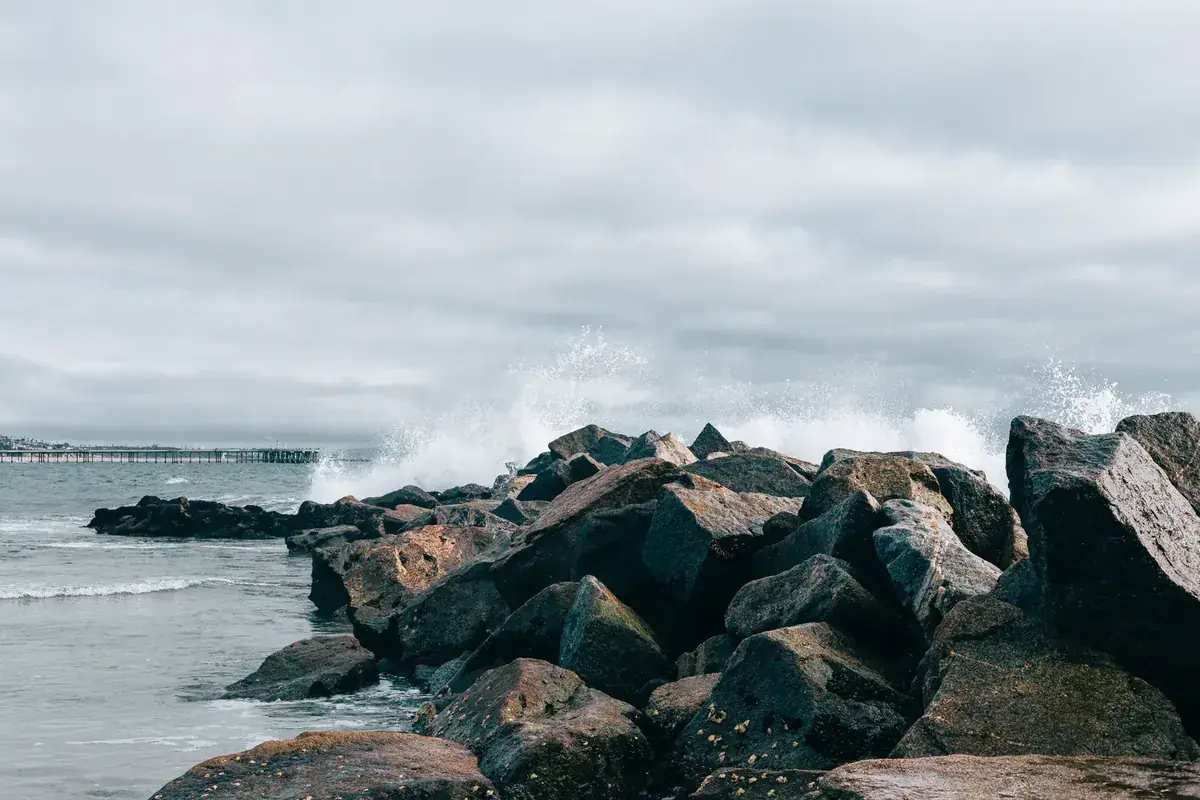 Waves wash over a rocky breakwater under a windy grey sky (Cancer and Libra compatibility)