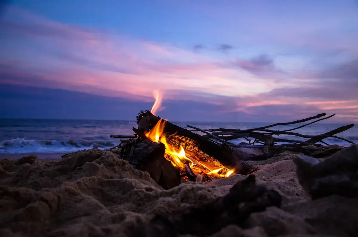 A driftwood bonfire burns on a beach as the sea fades to dusk (Aries and Pisces compatibility)