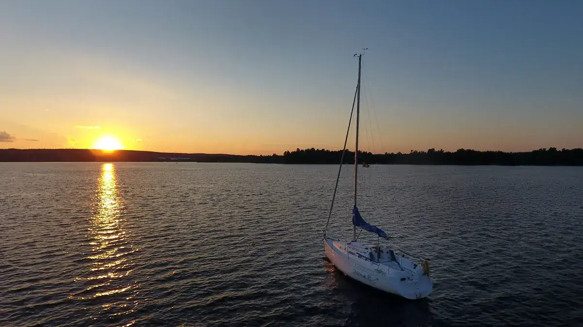 A sailboat rests on still water as the sun sets behind it (Leo and Pisces compatibility)