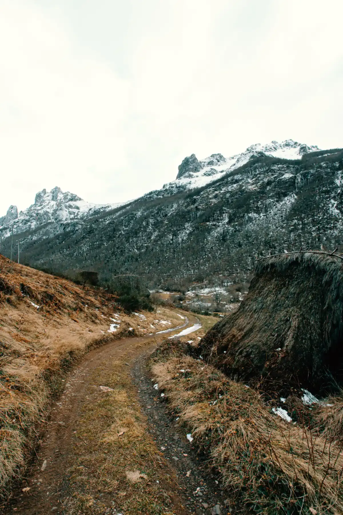 A narrow trail climbs a rocky mountainside beneath snowy peaks (Gemini and Capricorn compatibility)