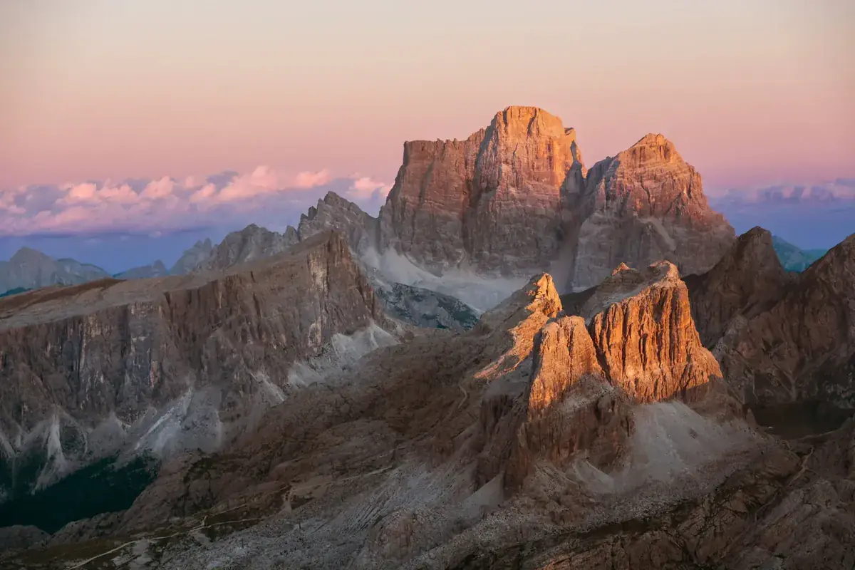 Jagged rock peaks glow orange in the last light above a sea of mountains (Aries and Capricorn compatibility)