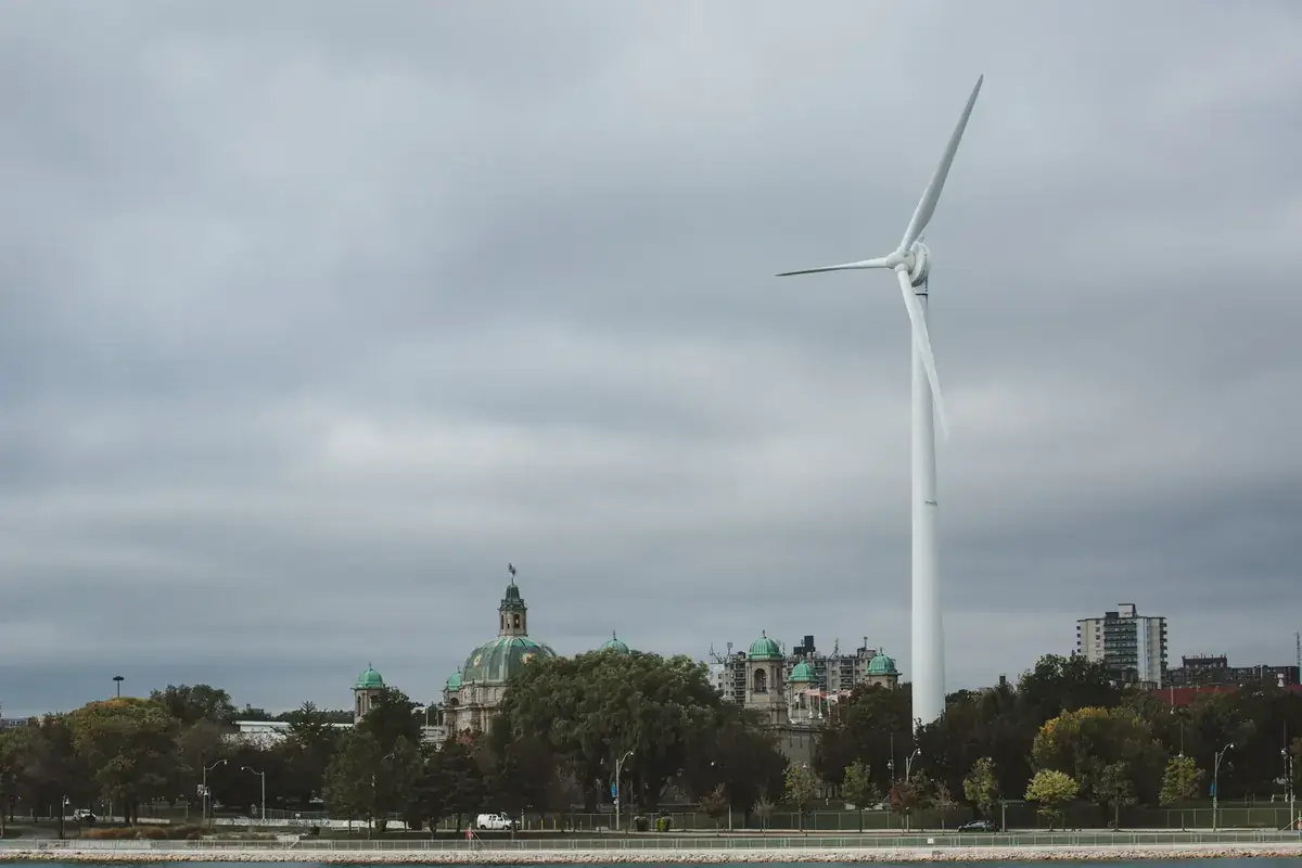 A lone wind turbine turns above a waterfront town under grey skies (Virgo and Aquarius compatibility)