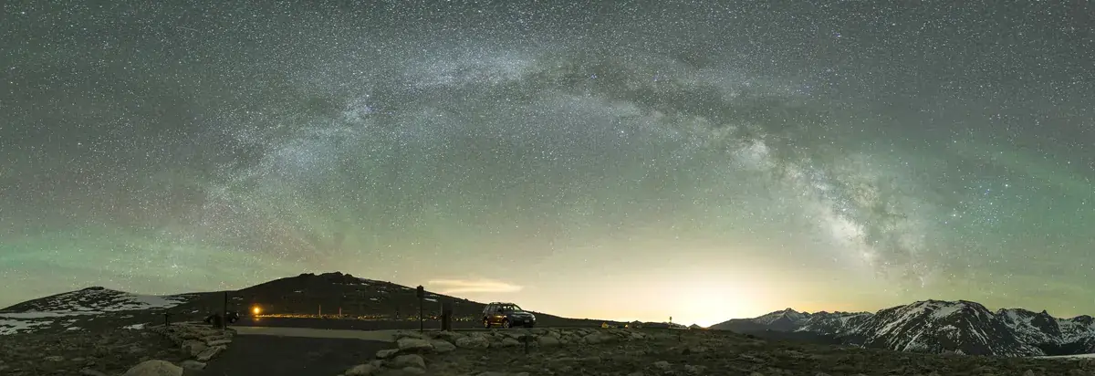 A panorama of the Milky Way over a turquoise night sky and distant peaks