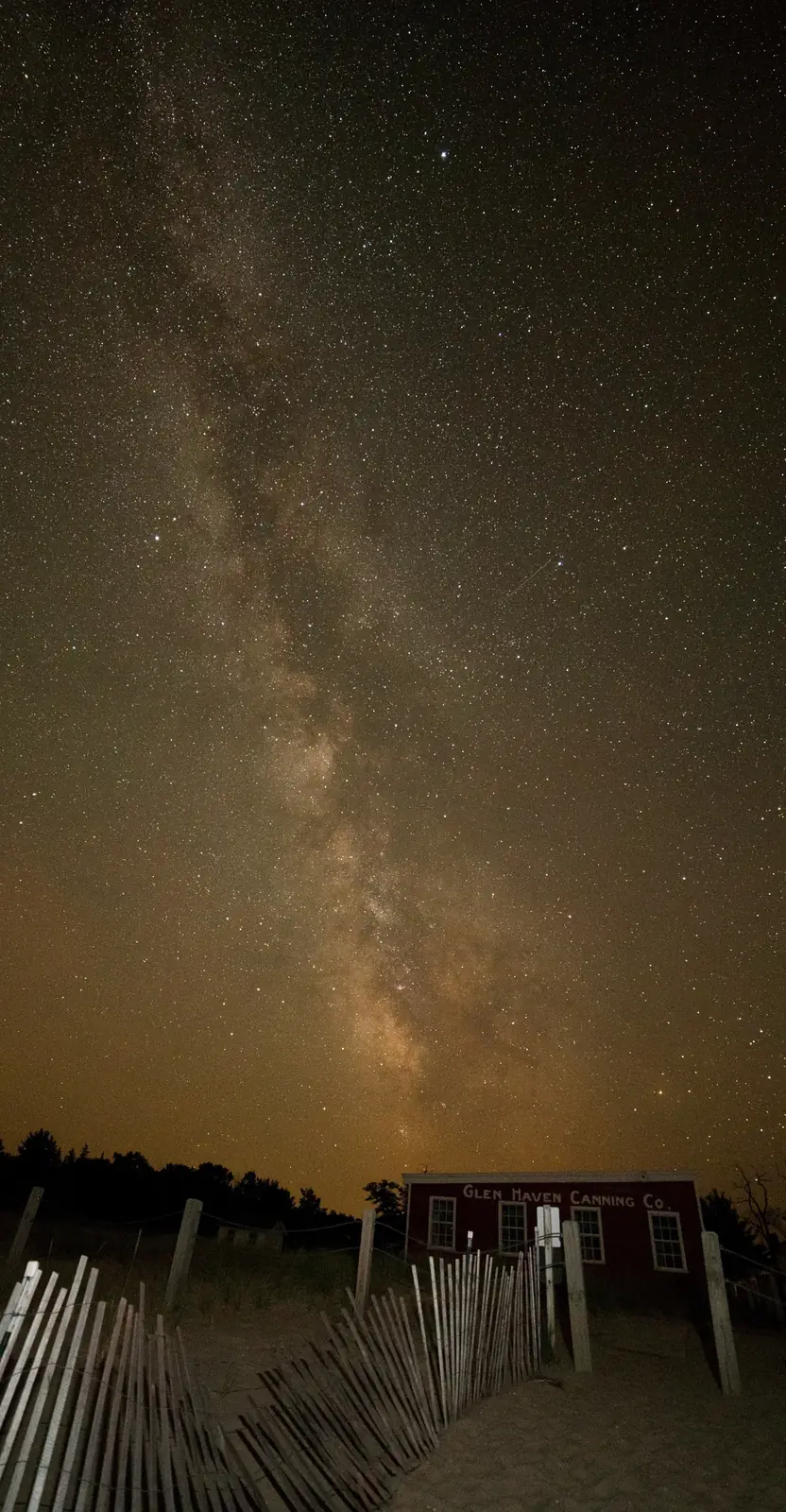 The Milky Way over a beach fence and a small red building