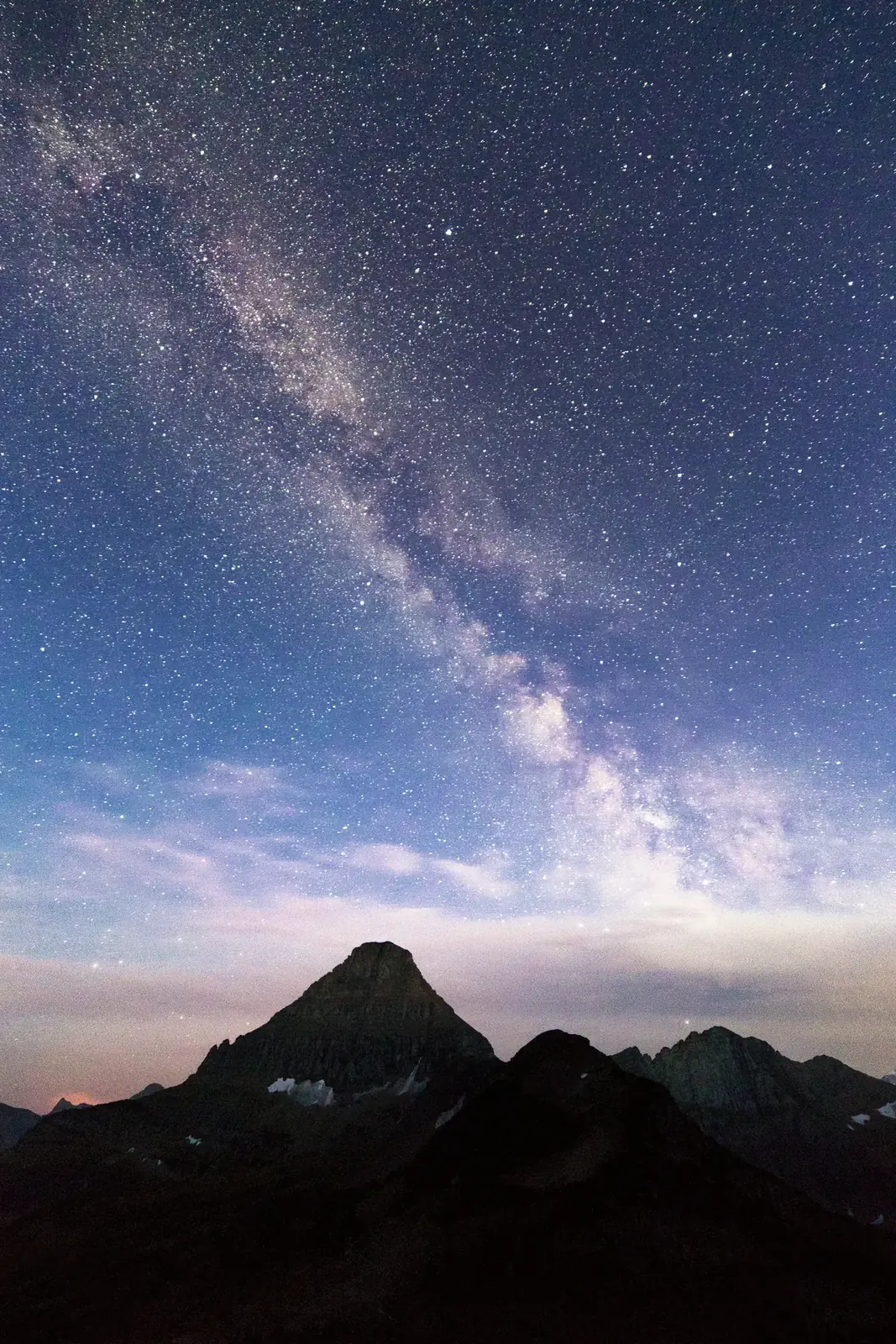 The Milky Way in a blue twilight sky above a pointed mountain peak
