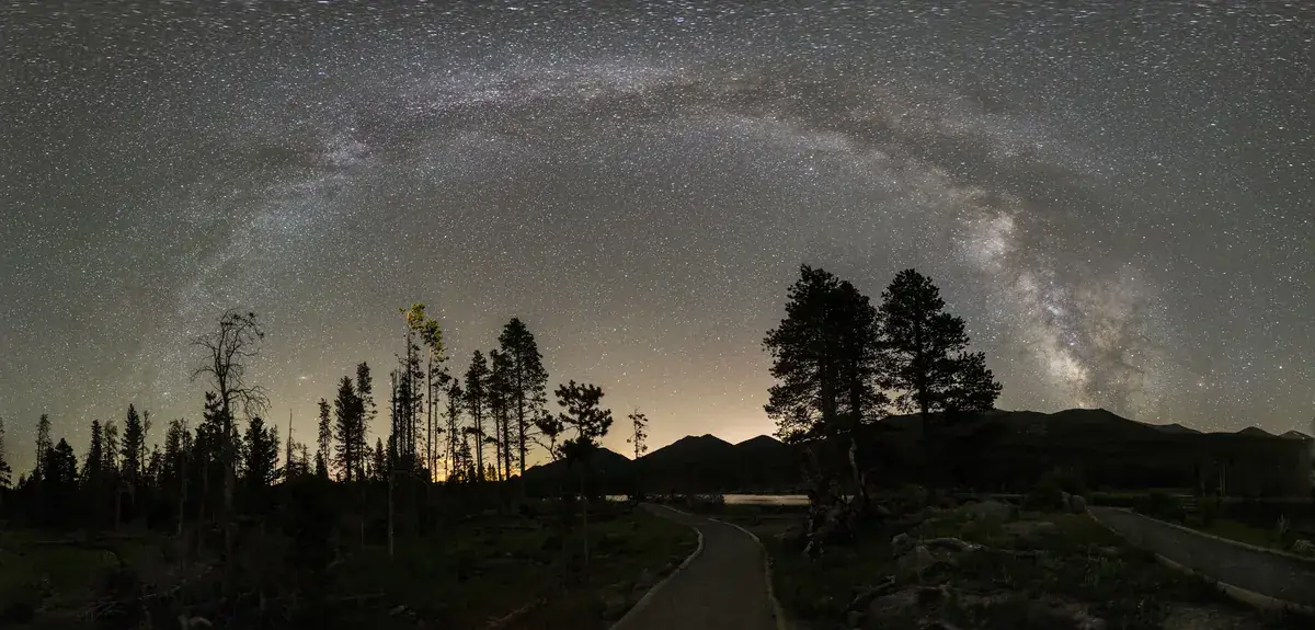 The arch of the Milky Way over a dark line of mountain trees