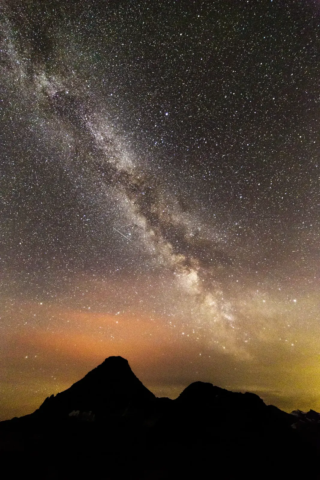 The Milky Way over dark peaks and an orange horizon glow