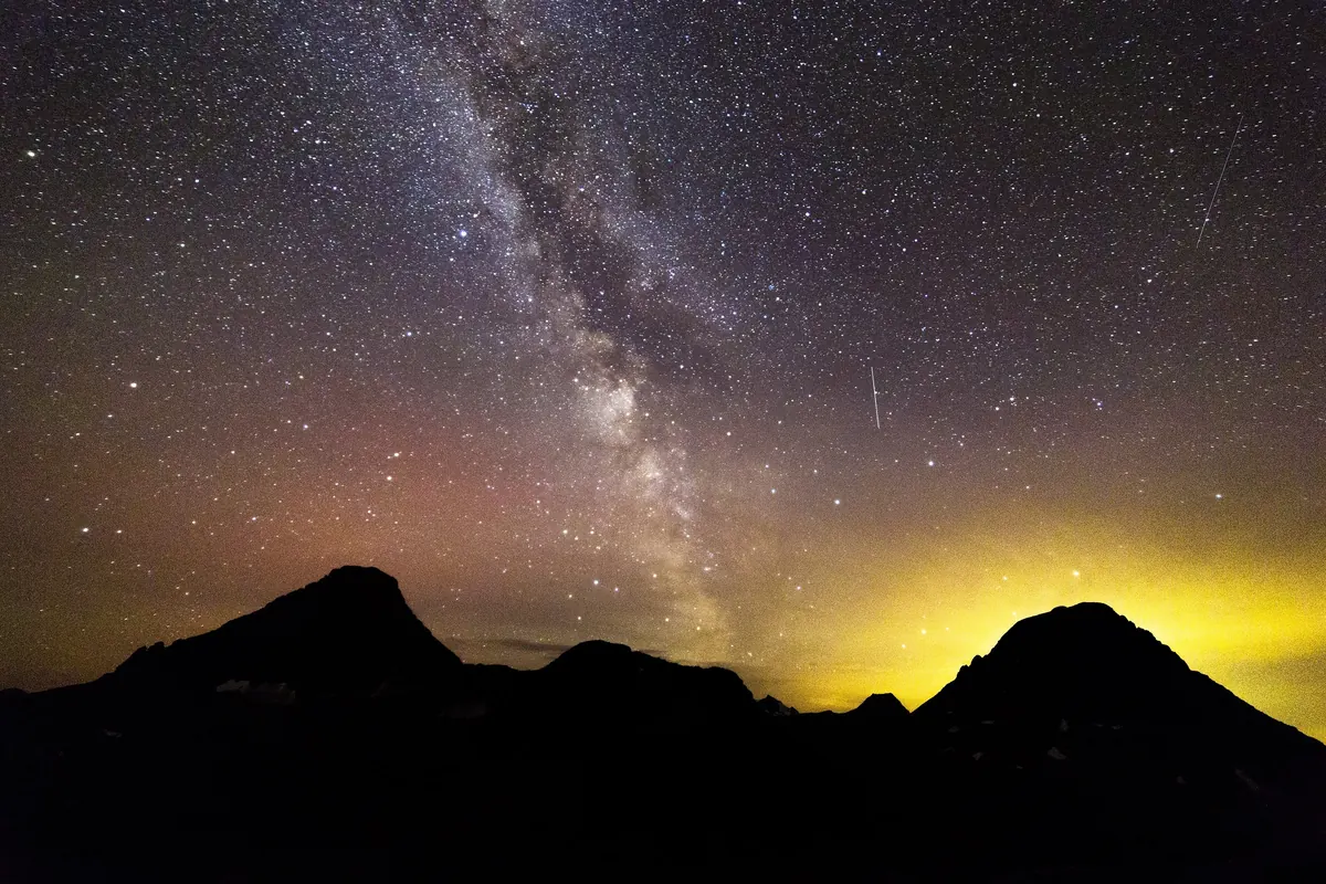 The Milky Way over a dark ridgeline and a yellow glow