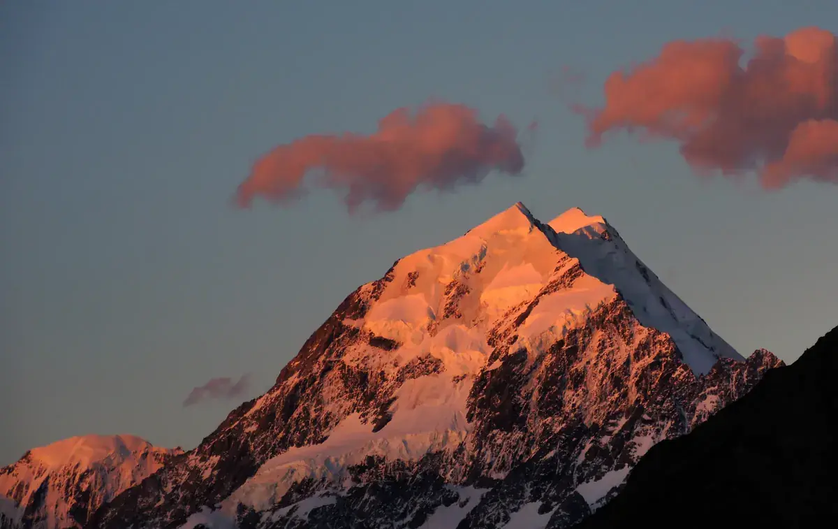 A snow peak lit pink by the last light, with pink clouds (Leo and Libra compatibility)