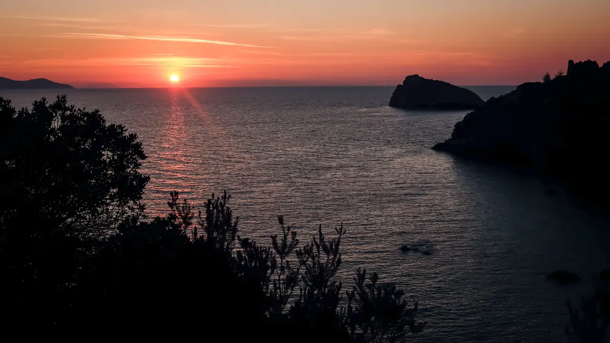 The sun setting into the sea beside a rocky headland (Scorpio and Pisces compatibility)
