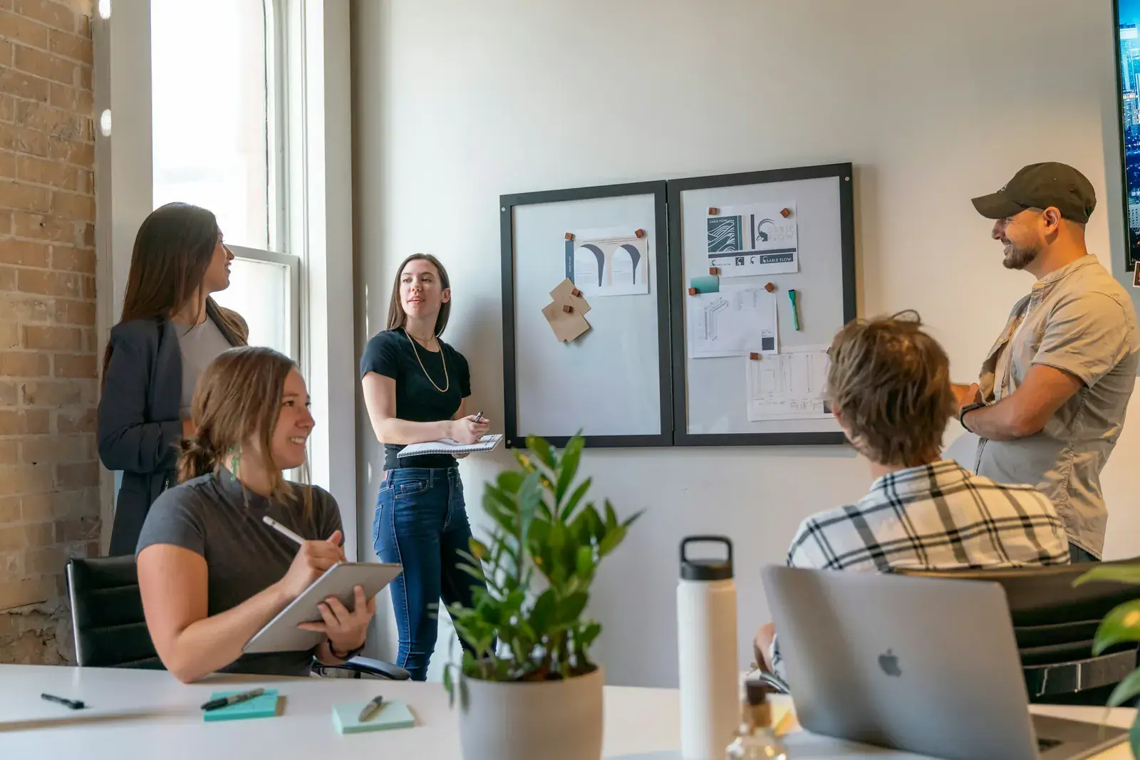 Colleagues gather around a whiteboard in a sunlit office meeting